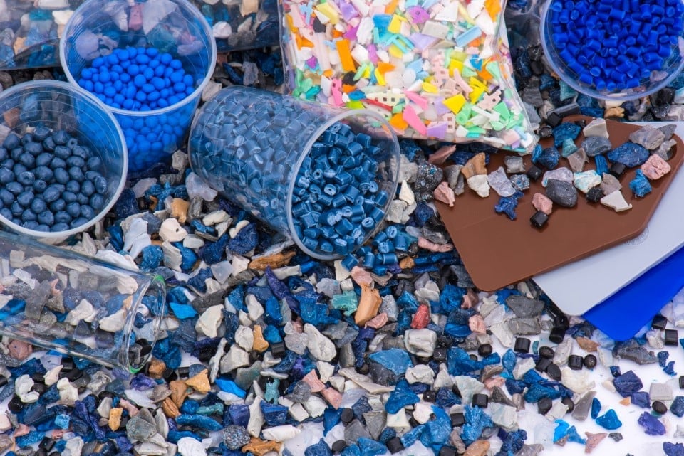Olika behållare med blå plastgranulat och återvunna plastbitar utspridda på en yta.