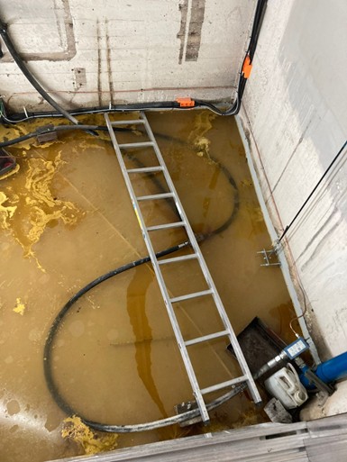Säkert arbete - icke godkänd: stegen ligger ner över kablar och skräp, golvet är vattenfyllt och stegen är svår att nå.