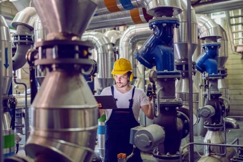 Pannoperatör med skyddshjälm justerar trycket för tryckkärl och läser instruktioner från en läsplatta.