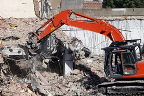 Excavator demolishing an old building structure amid debris