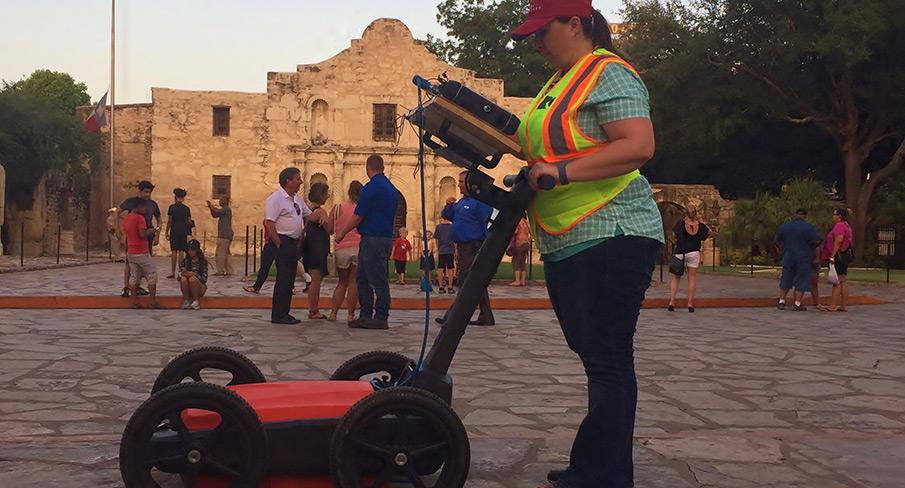 A Kiwa engineers in a safety vest operates ground-penetrating radar equipment in front of the historic Alamo mission in San Antonio, Texas, with people walking in the background