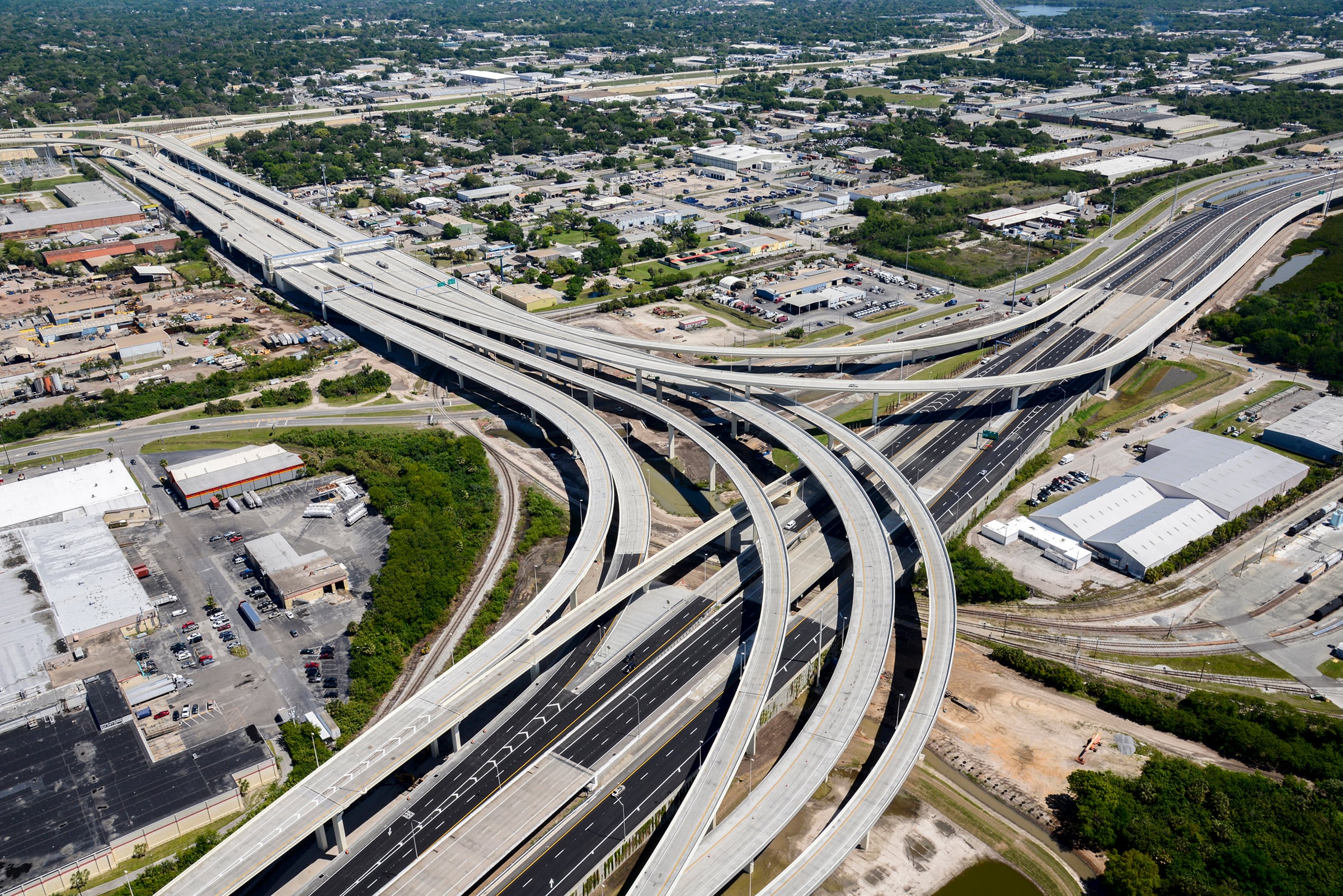 Aerial view of a busy highway interchange with multiple lanes and vehicles in motion, surrounded by green spaces, showcasing transportation infrastructure.