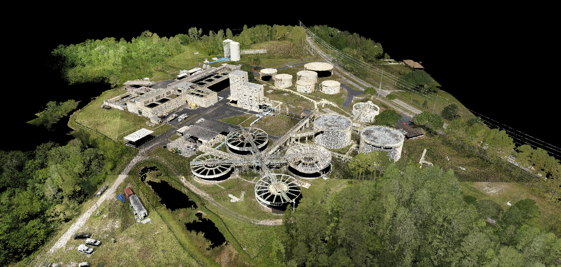 Aerial view of an industrial wastewater treatment plant with circular clarifiers, tanks, buildings, roads, and surrounding trees.