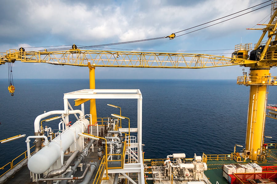 Yellow offshore crane and industrial equipment on an oil platform above the ocean under a cloudy sky.