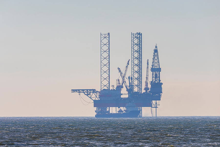 Offshore oil drilling rig in the ocean with tall cranes and steel towers against a hazy sky.