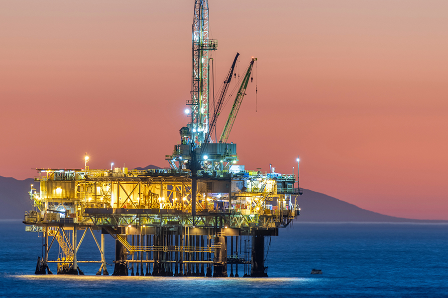 Oil and gas offshore platform lit up at sunset with cranes over the ocean.