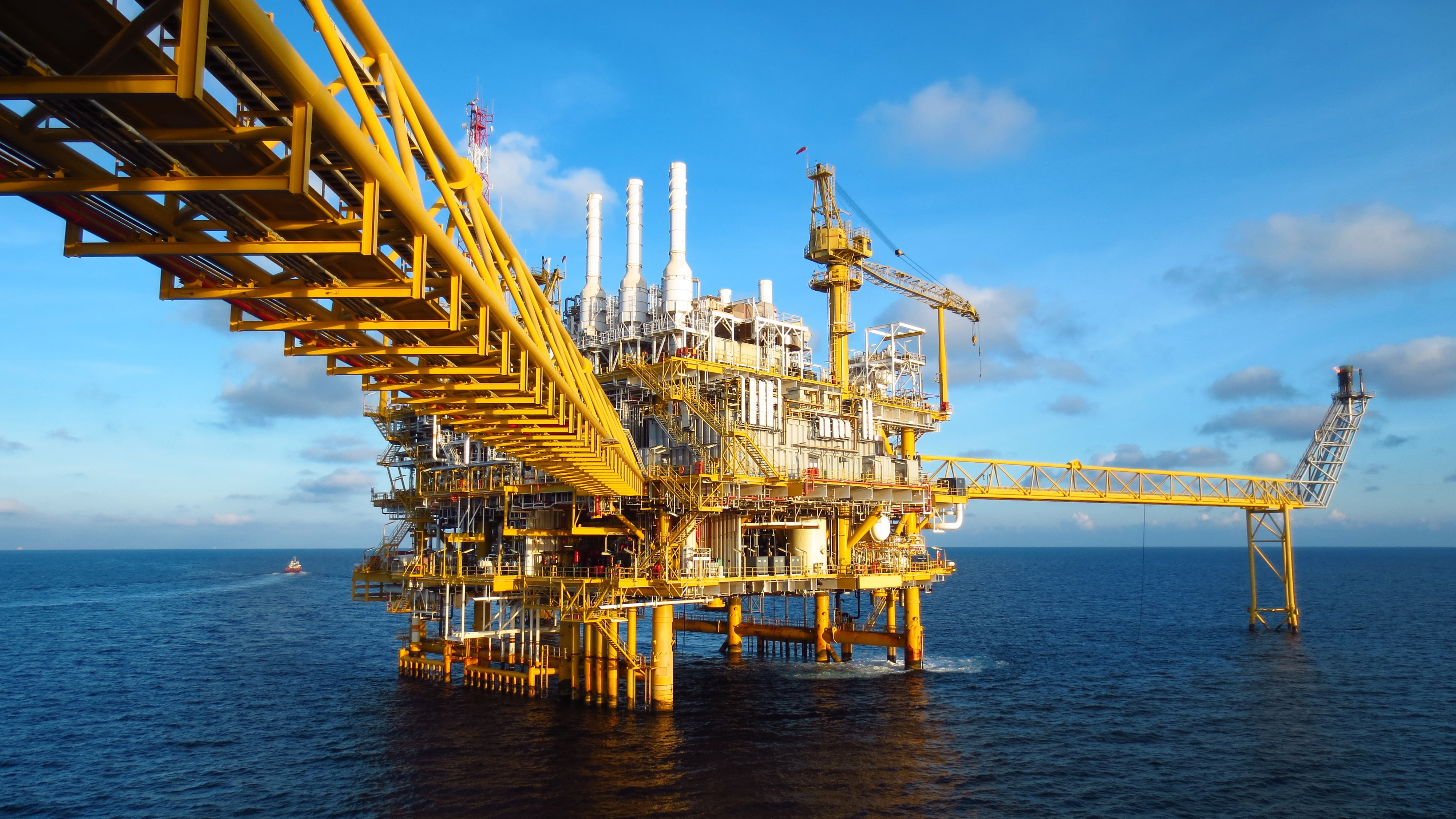 Offshore oil rig platform with yellow industrial structures in the ocean under a blue sky.