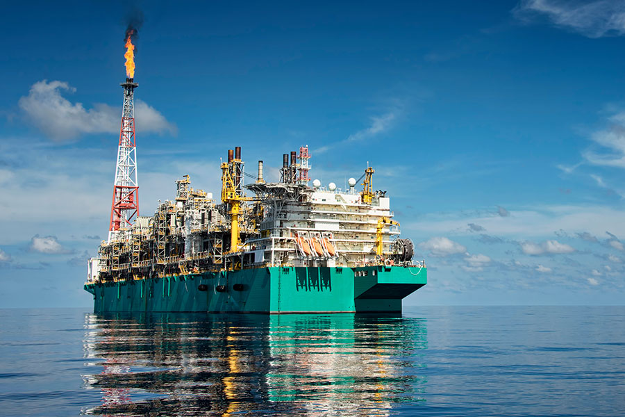 Offshore oil and gas platform with a gas flare above calm ocean water under a blue sky.
